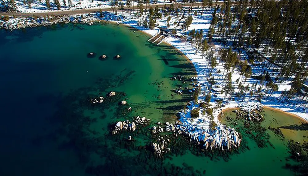 An aerial view shows the striking contrast between the deep blue waters of a lake the surrounding snow-covered landscape dotted with trees and a small beach area