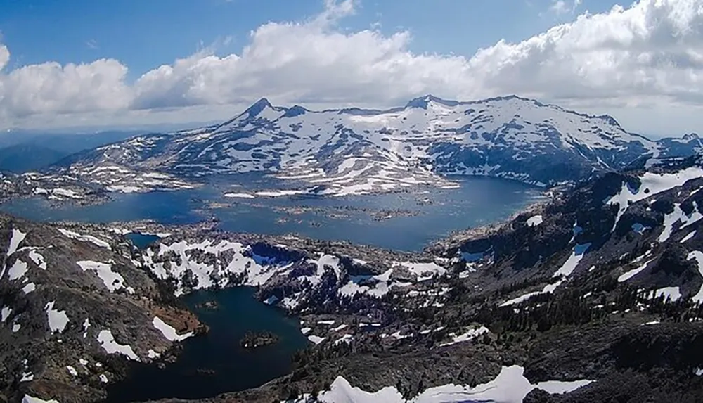 This is an aerial view of a mountainous landscape with snow patches and several lakes nestled among the peaks under a partly cloudy sky