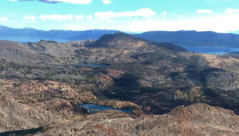 The image shows a rugged landscape with patchy vegetation several lakes and distant mountains under a partly cloudy sky