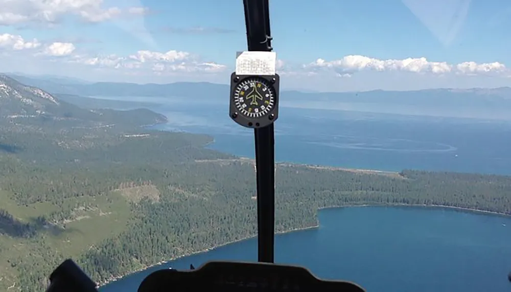 The image shows the view from a helicopter cockpit with a focus on an altitude indicator overlooking a scenic landscape featuring a large lake and surrounding forests