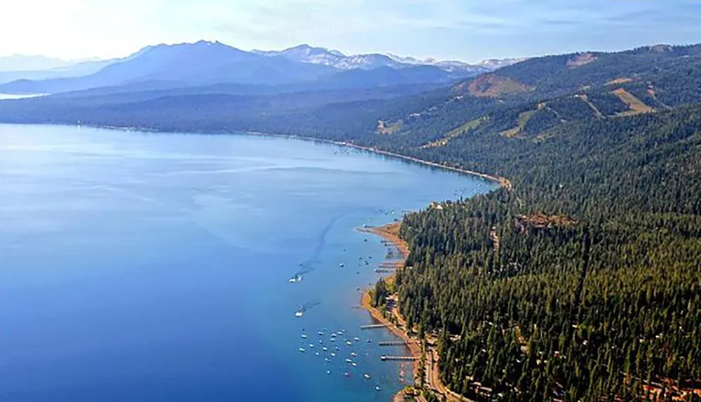 The image shows a picturesque aerial view of a clear expansive blue lake surrounded by lush green forests with mountains in the background