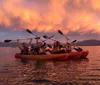 People in colorful kayaks enjoy a serene paddle on calm water under a dramatic orange sunset sky