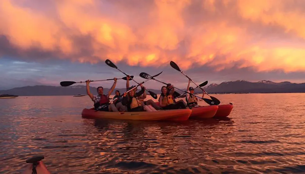 A group of people are kayaking on calm waters under a vividly colored sunset sky