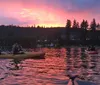 People in colorful kayaks enjoy a serene paddle on calm water under a dramatic orange sunset sky