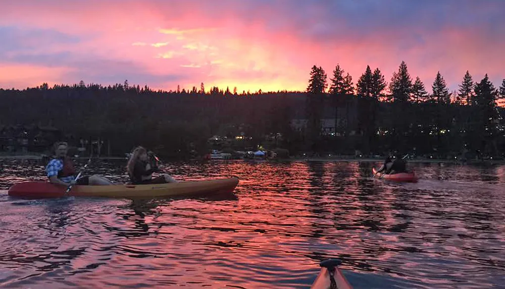 Kayakers are enjoying a serene sunset on a calm lake with vibrant pink and orange hues in the sky reflecting on the water