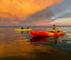 People in colorful kayaks enjoy a serene paddle on calm water under a dramatic orange sunset sky