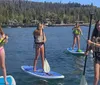 Four people are paddleboarding on a calm lake with a backdrop of a lakeside community and forested hills