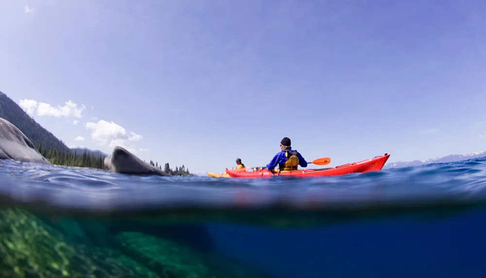Two individuals are kayaking on a clear blue lake with a split view showing both above and below water