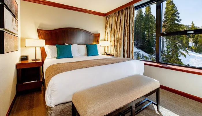 The image shows a cozy well-appointed hotel room with a large bed elegant decor and a scenic view of a snowy forest through the window