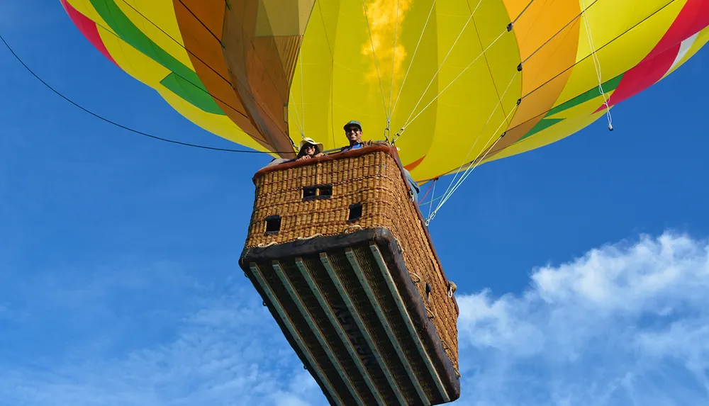 A colorful hot air balloon floats against a blue sky with two people visible in the basket