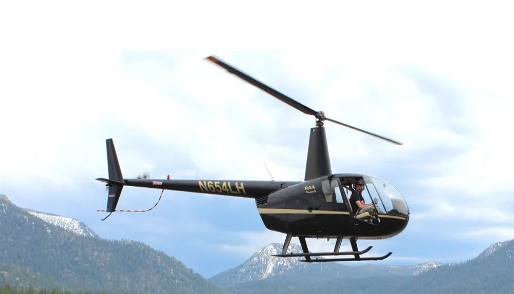A helicopter with the registration N654LH is flying near mountainous terrain with a visible pilot