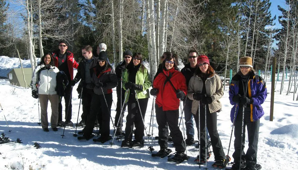 A group of smiling people equipped with snowshoes are standing together in a snowy environment likely enjoying a winter outdoor activity