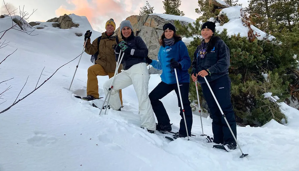 Four individuals are posing with smiles and trekking poles on a snow-covered slope during what appears to be a winter hiking excursion