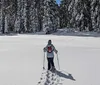 Three hikers are trekking through a snowy forest with the lead hiker smiling at the camera