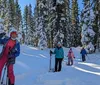 Three hikers are trekking through a snowy forest with the lead hiker smiling at the camera