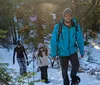 Three hikers are trekking through a snowy forest with the lead hiker smiling at the camera