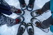 A group of people wearing snowshoes are standing on snow, forming a circle with their feet pointing towards the center.