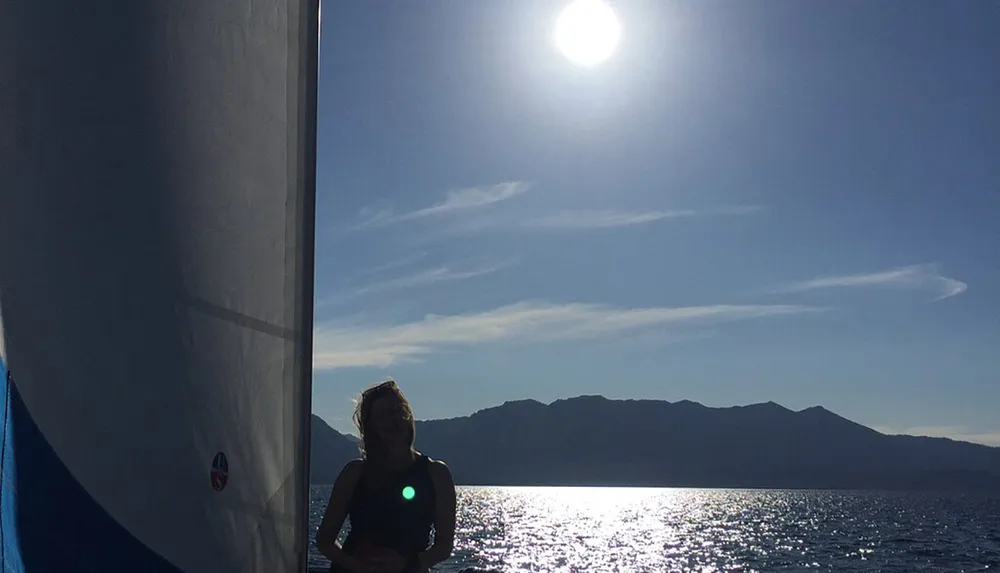A person is sailing on a sunny day with a clear sky captured in silhouette against the backdrop of the sea and a mountain range