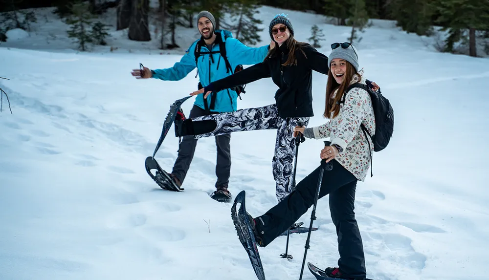 Three people are playfully posing with their snowshoes on a snowy trail exuding happiness and companionship