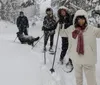 Two children and a dog are enjoying playing in the snow with one child lying down and another sitting both are wearing winter gear while the dog stands beside them