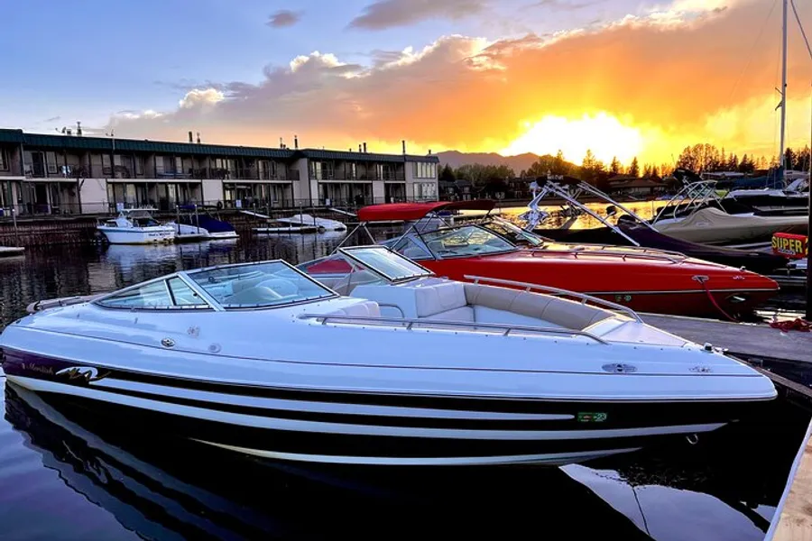 The image shows a serene marina scene with boats moored in calm water, against the backdrop of a beautiful sunset and residential buildings.