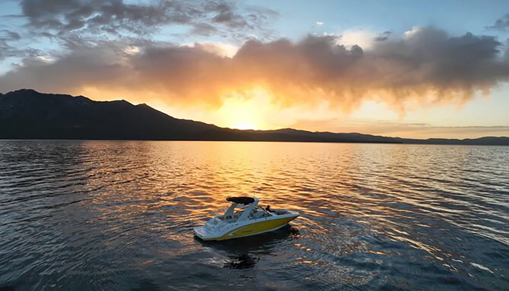 A jet ski floats on calm waters with a backdrop of a dramatic sunset over mountainous terrain