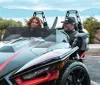 Two individuals are enjoying a ride in a Polaris Slingshot against a backdrop of nature