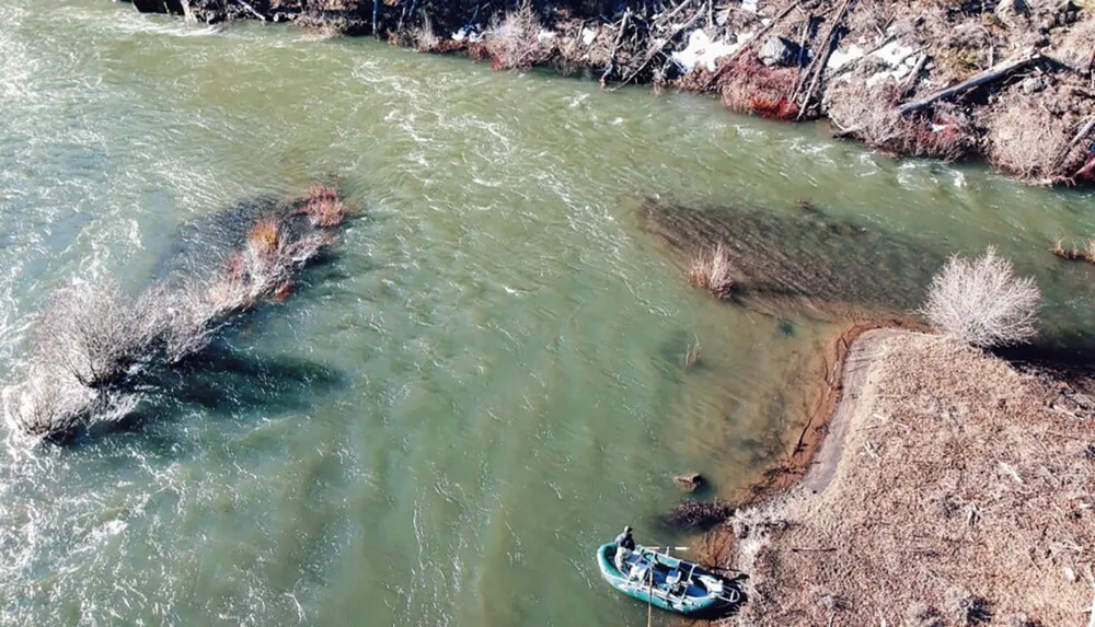 An aerial view of a person in a small boat on a river near a wooded riverbank