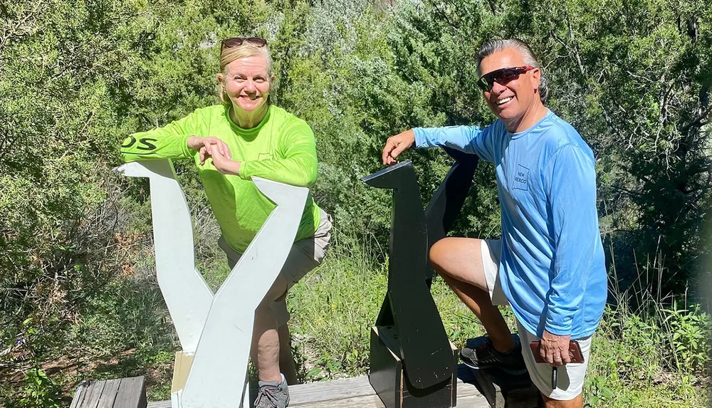 Two people are posing with large three-dimensional letters Y and K in a sunny green outdoor setting