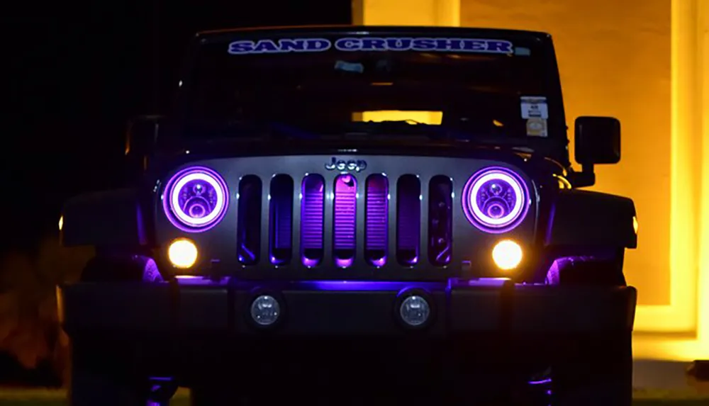 A Jeep with the label SAND CRUSHER on its windshield glows with purple lights around its headlights at night