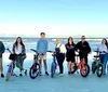 Four people are smiling for a photo on a sandy beach with bicycles two of which have signs saying Rent Me indicating they may be rental bikes