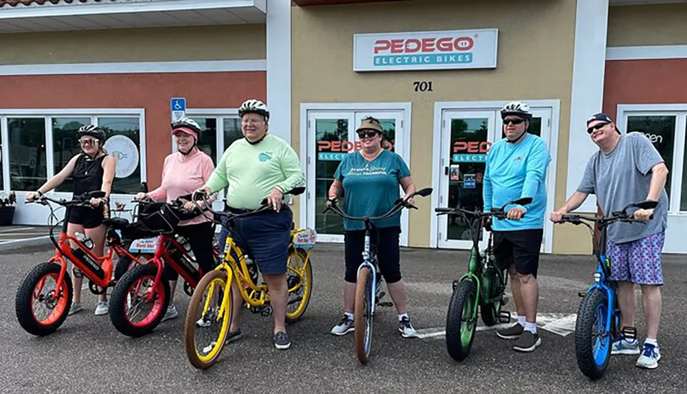 A group of six people is smiling for the camera while standing with their colorful electric bikes in front of a Pedego Electric Bikes store