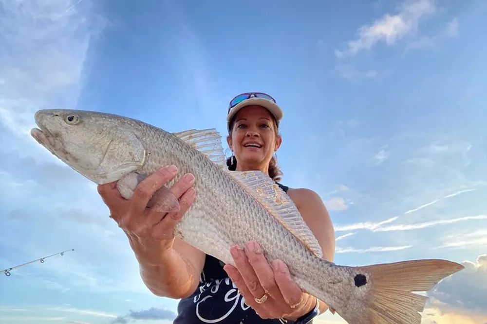 A smiling person is proudly holding a large fish with a cloudy sky in the background
