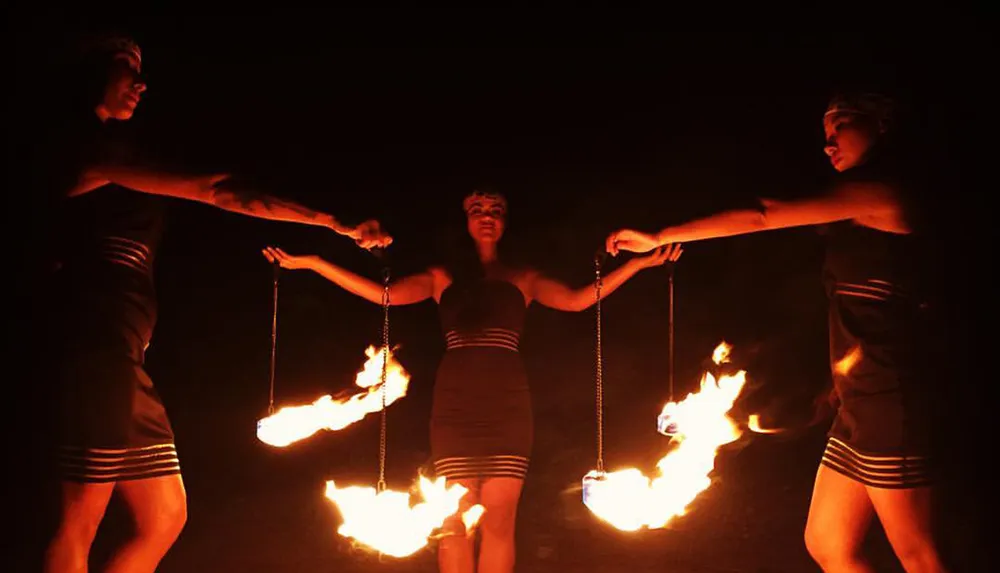 Three performers are holding flaming poi during a nighttime fire dance
