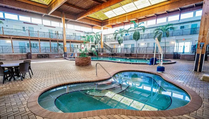 An indoor swimming pool area with a hot tub surrounded by two levels of hotel balconies brick flooring and tropical plants under a wooden ceiling