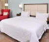 The image shows a neatly made king-sized bed with white bedding in a tidy hotel room accompanied by a red accent chair and contrasting modern lamps