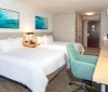 The image shows a modern and neat hotel room with two beds aquamarine-themed wall art and a workspace