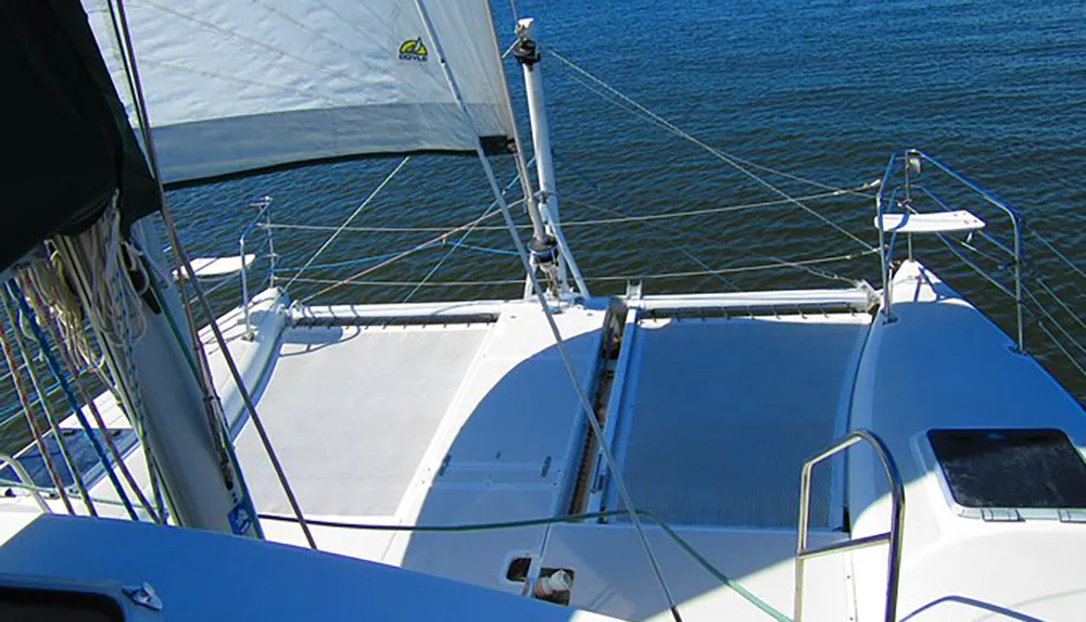 The image shows a view from the deck of a sailing catamaran with its sails hoisted gliding over the water