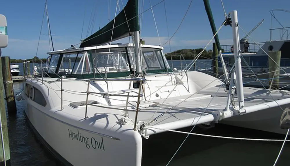 A white sailboat named Howling Owl is docked at a marina under a clear blue sky
