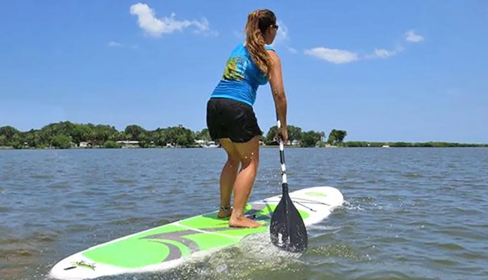 A person is stand-up paddleboarding on a sunny day on a calm body of water
