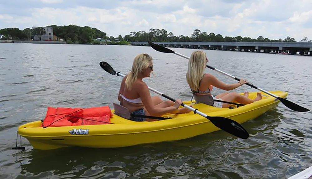 Two individuals are kayaking together in a yellow tandem kayak on calm waters