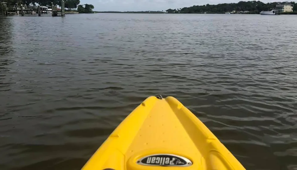 The image shows the bow of a yellow kayak on the water with a view of docks and waterfront houses in the distance