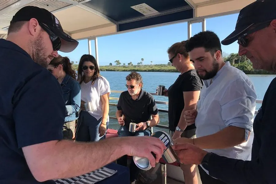 A group of people are gathered around on a boat, with one person pouring a drink from a can.