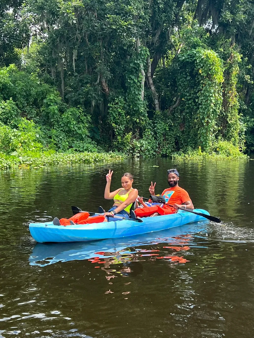 Two people are happily kayaking on a calm river surrounded by lush greenery