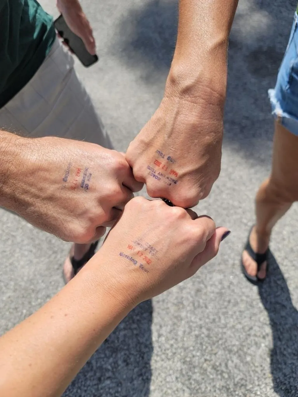 Three people have joined hands with each of their wrists stamped with a purple ink stamp possibly indicating entry to an event or venue