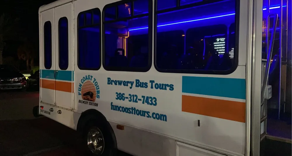The image shows the side of a parked white shuttle bus with blue interior lighting branded for Fun Coast Tours - Brewery Bus Tours with contact information and a website listed on its exterior