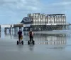 Two people ride Segways on a wet beach with a large pier structure in the background