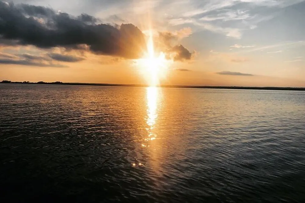 The image shows a serene sunset with golden rays beaming through the clouds and reflecting on the calm waters of a lake or sea