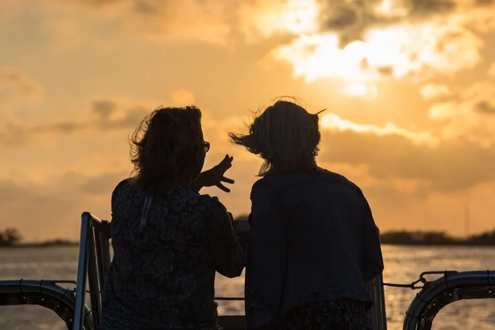 Two people are silhouetted against a sunset as they engage in conversation aboard a boat