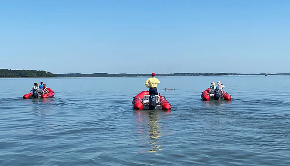 Several people are leisurely riding in inflatable red boats on a calm blue lake